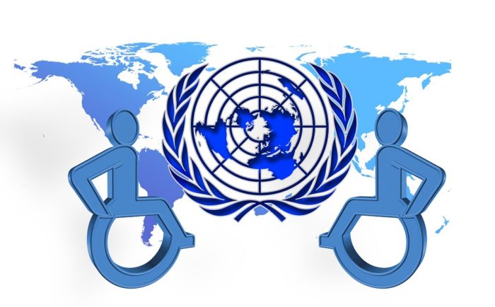 Two wheelchair user symbols overlying world map, with UN symbol in centre