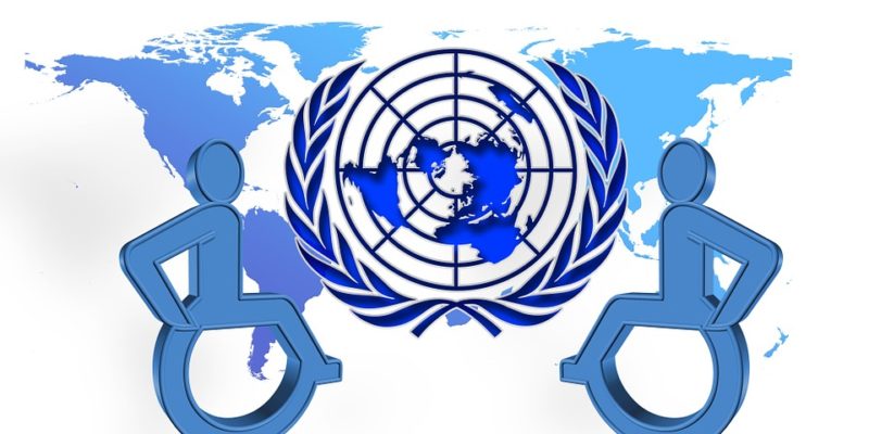 Two wheelchair user symbols overlying world map, with UN symbol in centre