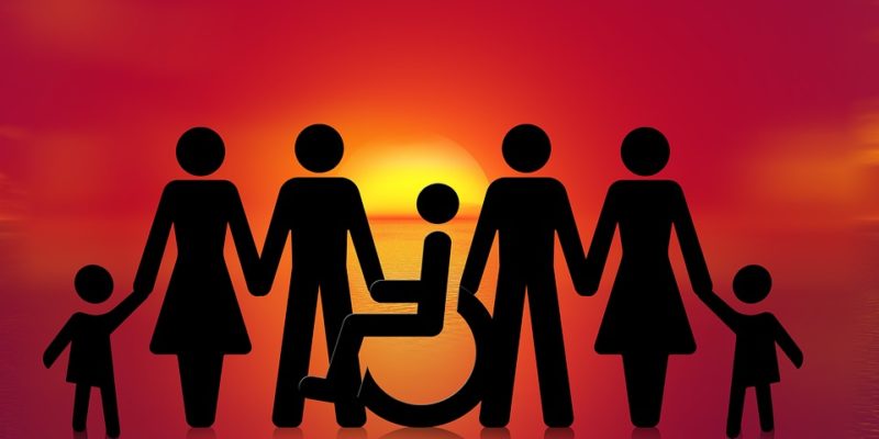 Sunrise background. Stick people, adults, children and in the centre a wheelchair user, hold hands. Image seeks to convey notion of inclusive future.