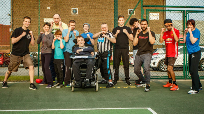 Group photo of Mixed Ability boxing session. Disabled and non-disabled participants stand in boxing pose. All look very cheerful!