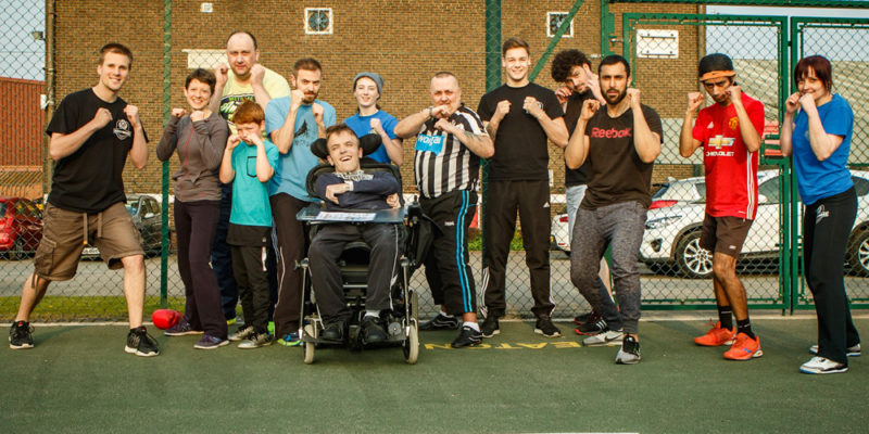 Group photo of Mixed Ability boxing session. Disabled and non-disabled participants stand in boxing pose. All look very cheerful!